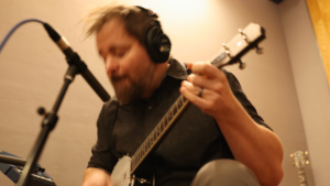 Stephen Vesolich playing the banjolele during the Psalm 126 recording session, captured with warm motion blur.