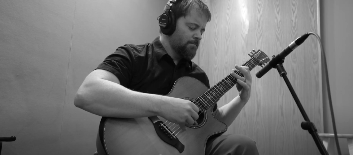Stephen Vesolich, the creator of The Mountains Surround, playing guitar